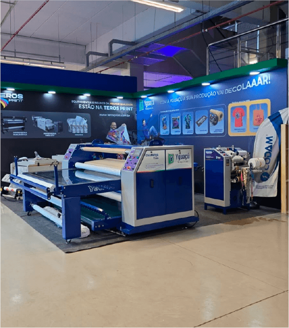 Mostra o estande da Yguaçú Máquinas com seus equipamentos de serigrafia, sublimação e DTF expostos, na COMTEX 2025.